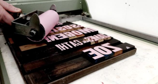 A an ink roller being used to coat wood type with pink ink.