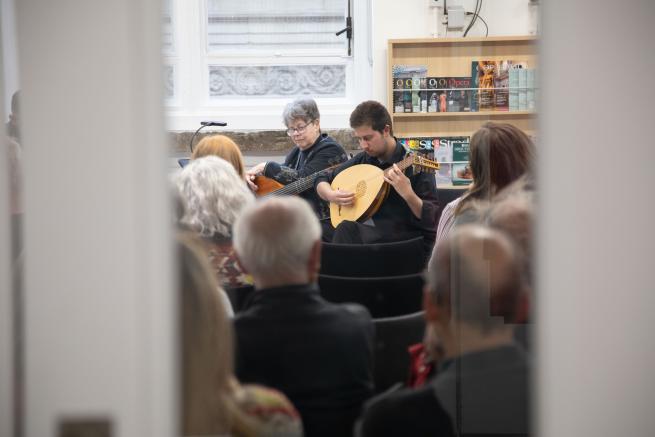 Person playing lute in crowd of people image taken through doorway