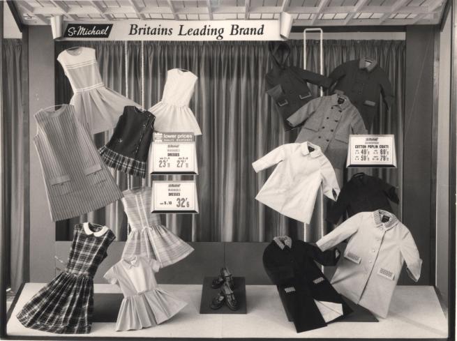 Black and white photo showing a window display of children's clothing