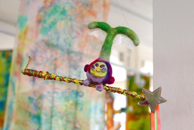 A felted beetroot with a grumpy live green face rides on top of a magic wand suspendd in the air.