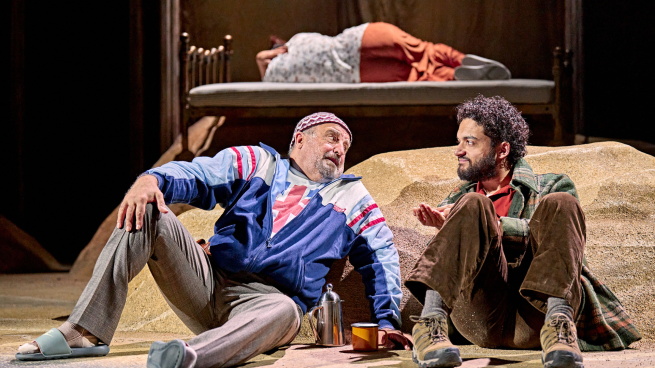 Two actors performing on stage. They are both sat on the floor.