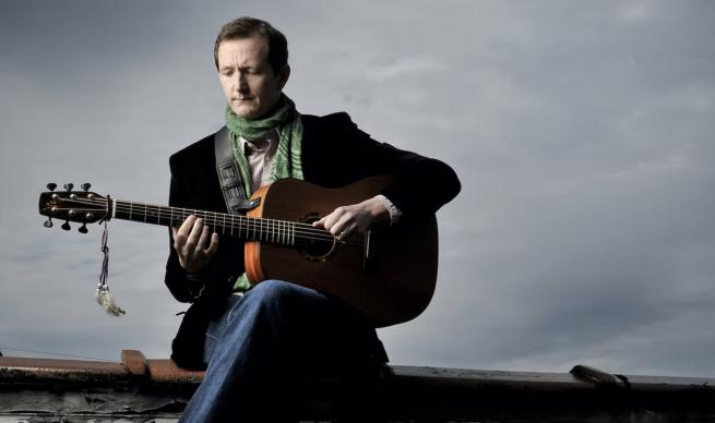 Man wearing black blazer playing guitar