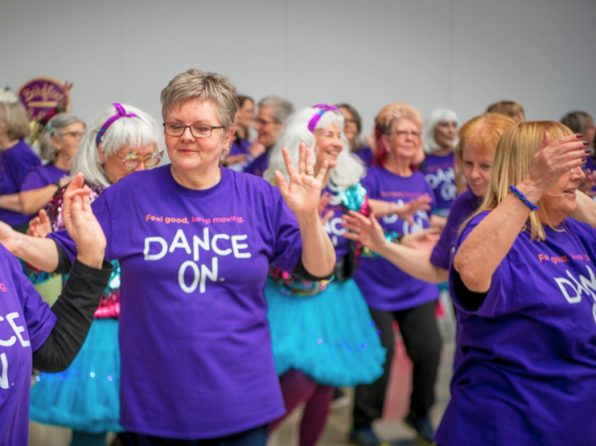 A group of women in 'dance on' T-shirts are dancing together 