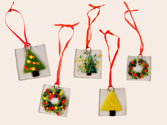 A photo of 5 Christmas tree glass ornaments. They have triangle Christmas trees and wreaths with red glass pebbles on clear glass.