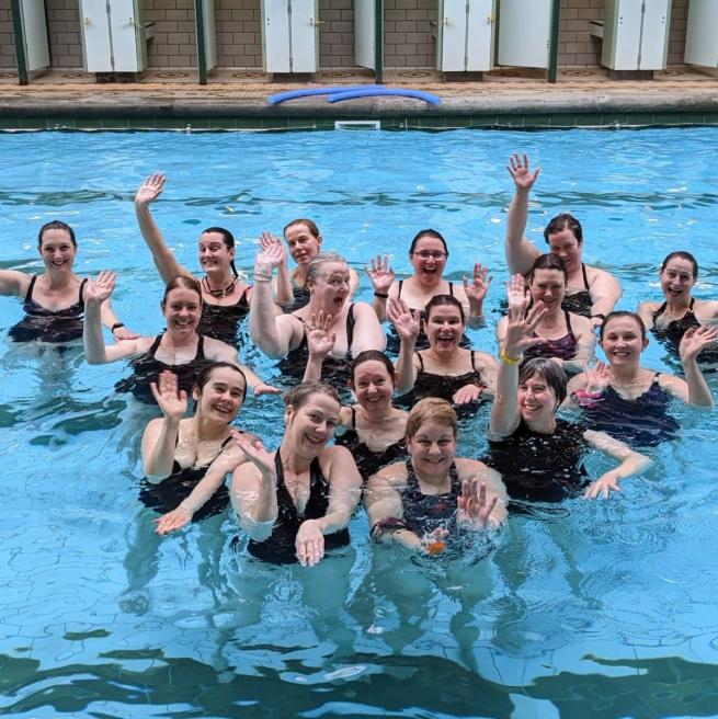 women in pool waving and smiling