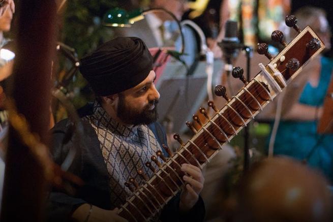 Opera North's poster for 'Orpheus'; A man wearing a turban with a sitar sits playing amongst a group of musicians.
