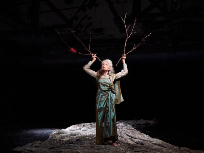 A woman stands in a river of silk with two sticks to her head like antlers