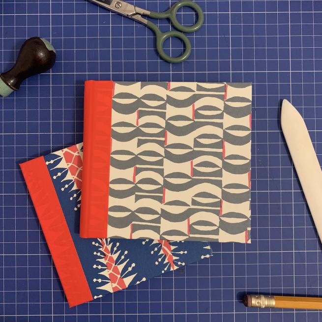 A photograph of two handmade notebooks on a blue cutting mat