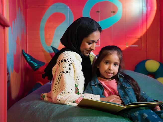 Mother and child reading a book in a cosy colorful setting.
