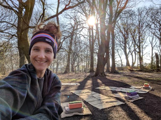 a woman smiling in a woodland surrounded by yoga mats