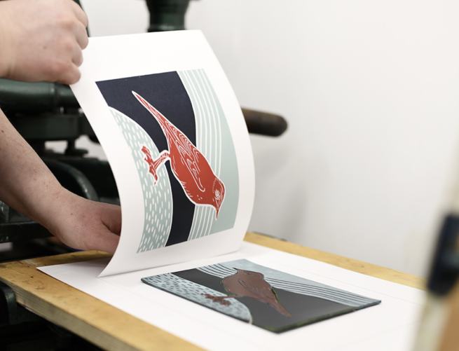 A lino cut image of a bird in red and black being revealed from the lino