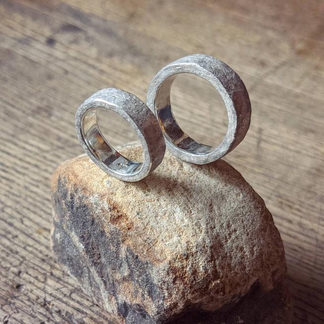 Two silver textured ring, sit on a stone on top of a wooden surface