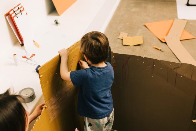 Young person exploring a cardboard box with the support of an adult