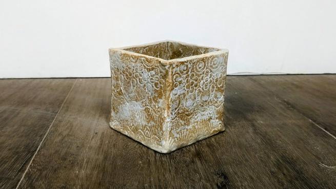 A photograph of a beige and white ceramic open top box on a wooden table
