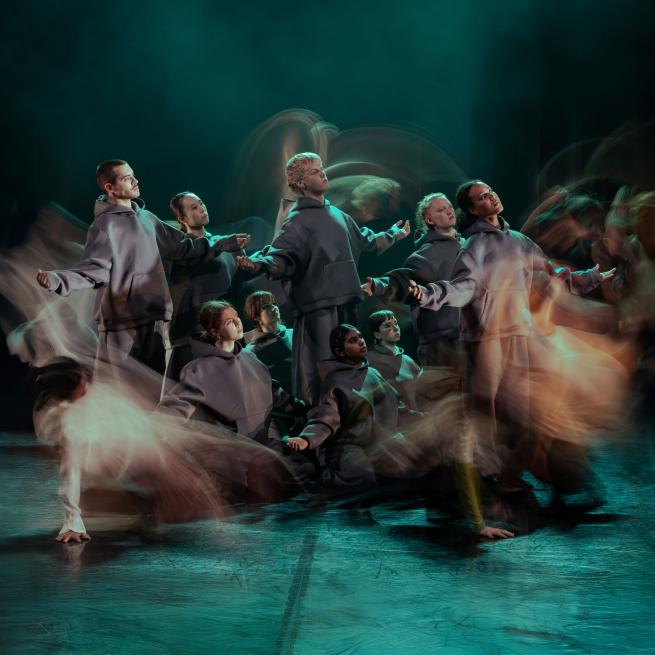 Group of dancers facing out to right with blurred dancers around