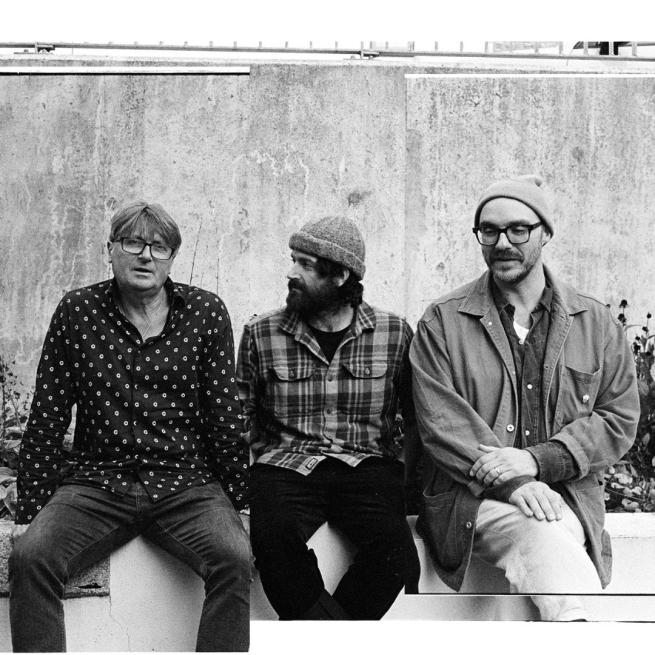 Black and white, textured, collage-style image of the three members of LYR sitting candidly on a brick wall.