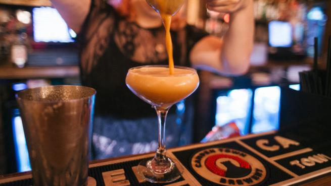 A close up shot of a cocktail being strained into a coupe glass.