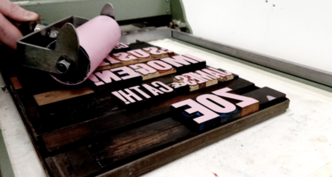A roller being used to apply pink ink to woodtype