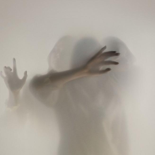 Three faint figures with outstretched arms reach out through thick grey mist.