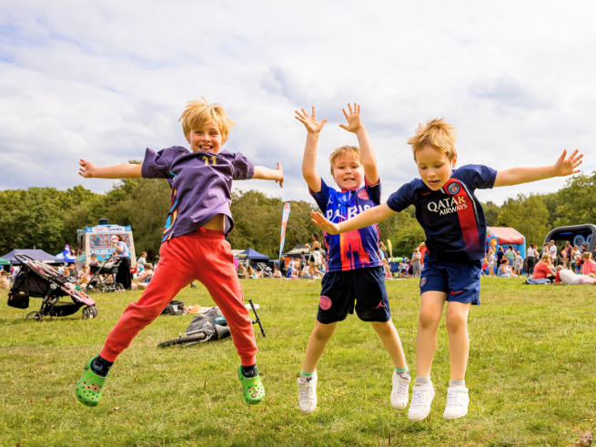 Three boys jumping in the air on a grass park in front of inflatables in the sunshine