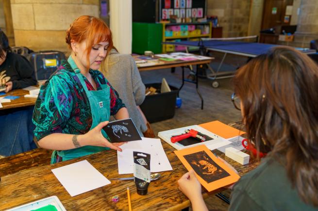 Two people taking part in the Make a Zine workshop, working with lino printing