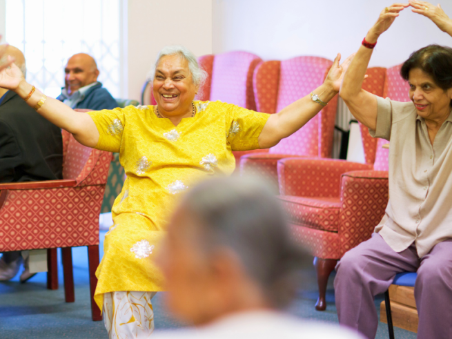 A lady in yellow looks extemely happy dancing in a chair 