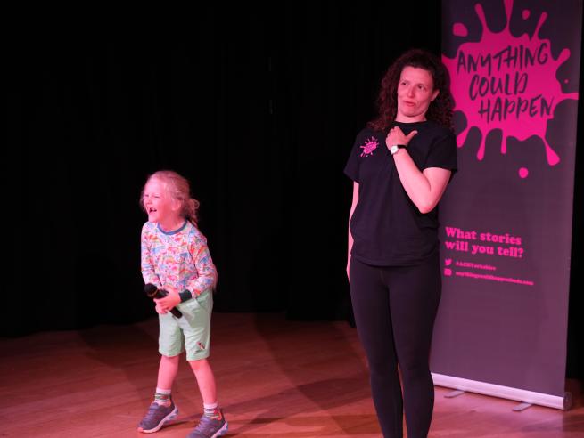 7 year old boy with a microphone laughs hysterically while a female performer pulls a funny face