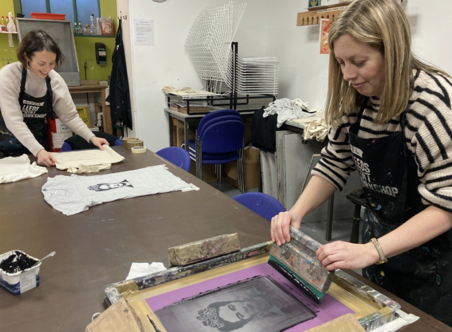 Two artists screen printing an image of Frida Kahlo onto a t-shirt