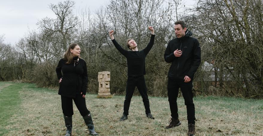 the actors in rehearsal dressed in black outdoors