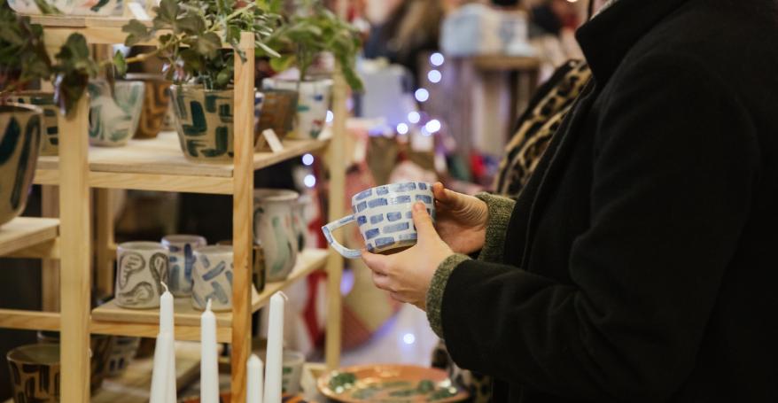 A woman holding a blue and white patterned ceramic mug over a stall covered in Clod Studio pottery