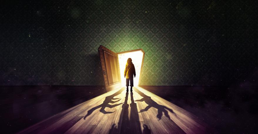 A young girl wearing a yellow anorak stands facing an open door. Bright light cascades out causing shadows across the old wooden floor. Two boney hands reach around the girl in the dark. Above the door, etched into green wallpaper, are the words ‘Coraline - A Musical’. 