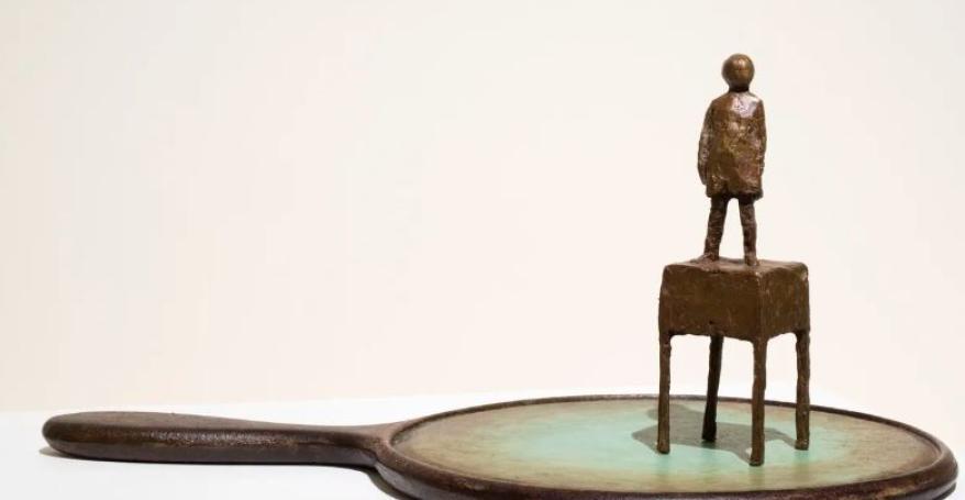 bronze statue of a child stood on a small desk, that looks like its stood on a old fashioned hand mirror