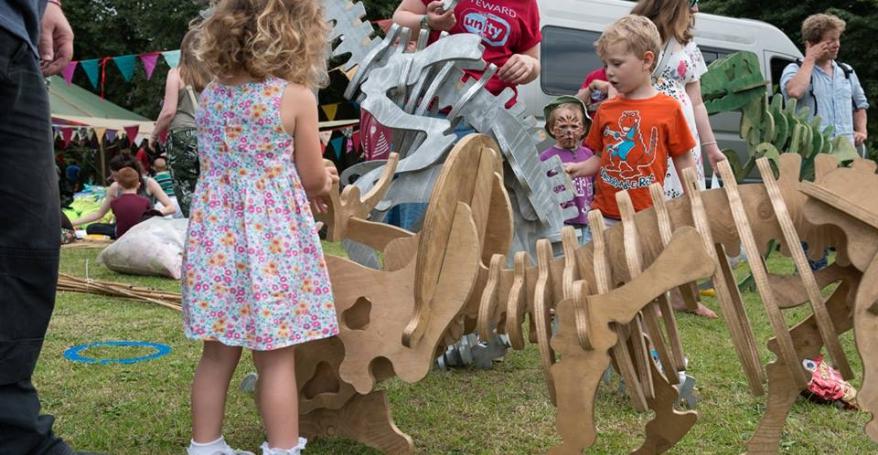 children outdoors with a wooden dinosaur fossil