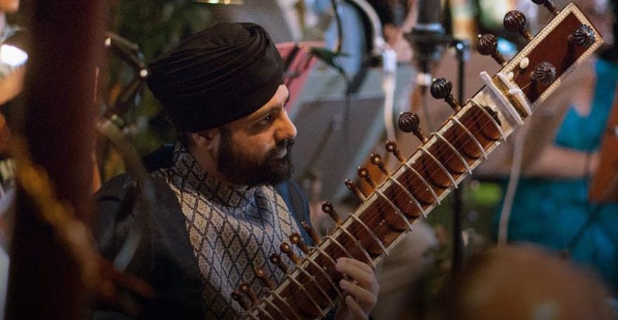 Opera North's poster for 'Orpheus'; A man wearing a turban with a sitar sits playing amongst a group of musicians.