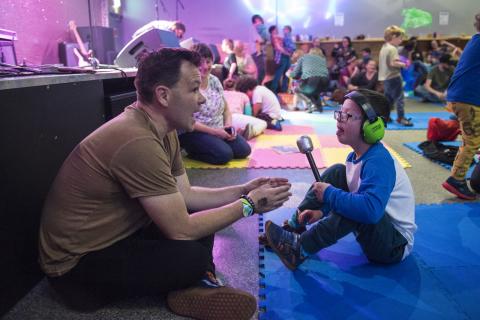 Adult man sat on floor with young boy who is wearing green ear defenders