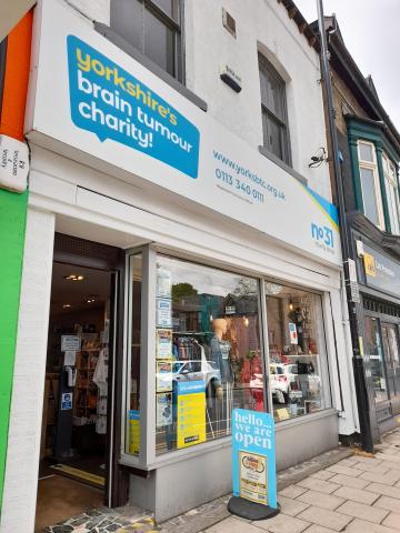 outside of Yorkshire's Brain Tumour Charity shop. A shop front painted white with a board outside that says we are open.