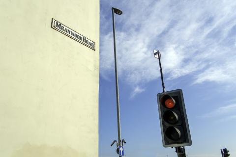 Traffic light and a wall with Meanwood Road sign on it and blue sky behind.