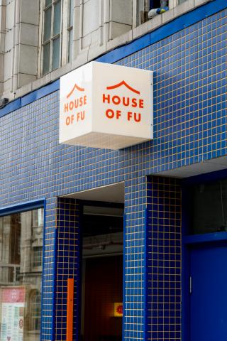 A white light-box, with orange writing reading 'House of Fu', attached to a blue tiled wall 