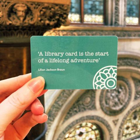 A hand holding a library card with the quote "A library card card is the start of a lifelong adventure" by Lilian Jackson Braun