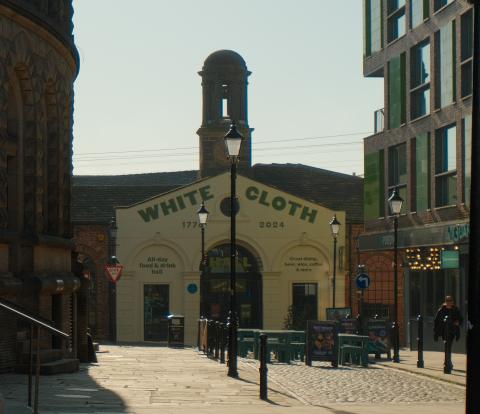 a cobbled street with tables and chairs and a building with large letters saying white cloth
