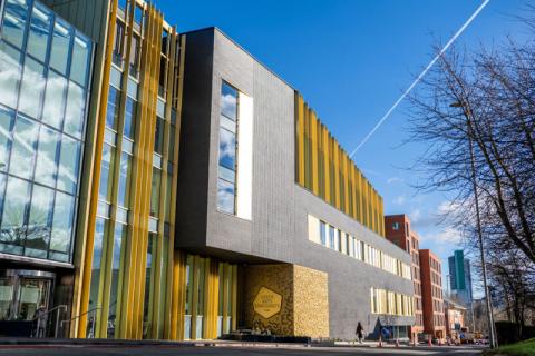 Gold and grey tall building alongside a road against a blue sky