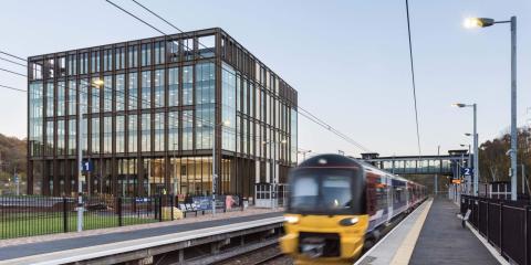 a train platform with a train blurred and a large glass building behind it