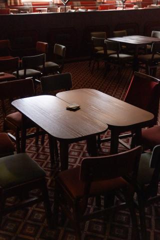 Dimly lit room with several wooden tables and chairs arranged casually. An empty, dark atmosphere is accentuated by scattered decks of cards on one table.