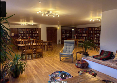 A room with bookshelf, cafe tables, chairs and couch.