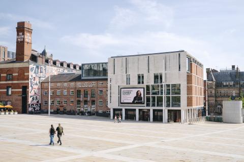 An exterior shot of the Carriageworks Theatre across Millennium Square, two people walk towards the theatre holding hands.