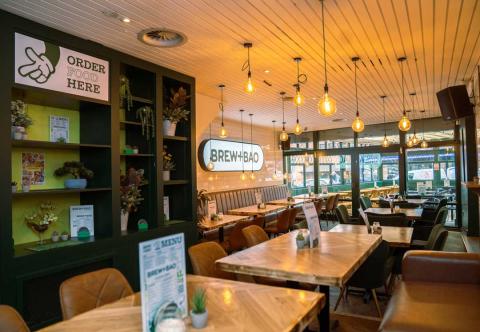 inside of a restaurant, wooden tables and leather chairs with a large window where there is outdoor seating