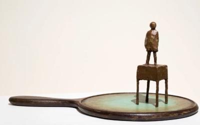 bronze statue of a child stood on a small desk, that looks like its stood on a old fashioned hand mirror