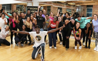 A group of people wave to the camera in a dance studio