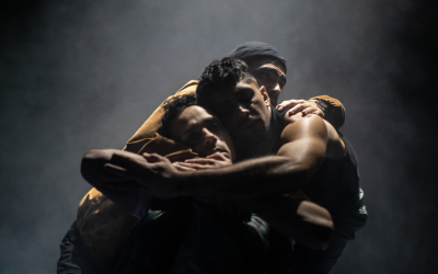 Three men embrace with their arms around each other. 