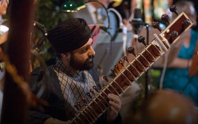 Opera North's poster for 'Orpheus'; A man wearing a turban with a sitar sits playing amongst a group of musicians.